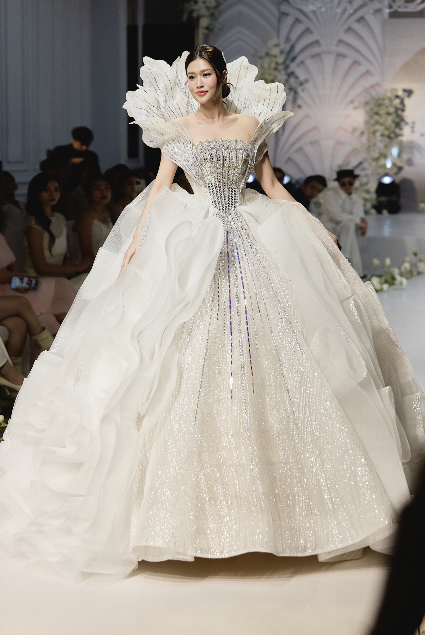 Kết bộ sưu tập, Hoa hậu Đoàn Thiên Ân xuất hiện với bộ váy cưới lộng lẫy, cầu kỳ, kiêu sa. NTK Kim Anh dựng gọng từ vai ra phía sau của váy, tạo thành những cánh hoa được cắt tỉa mềm mại nhưng vẫn đầy quyền lực, tựa như ánh hào quang làm rực sáng. Hình ảnh các cô dâu hiệu đại – độc lập – tự chủ, đó chính là ý tưởng mà NTK Kim Anh hướng đến thông qua thiết kế này.