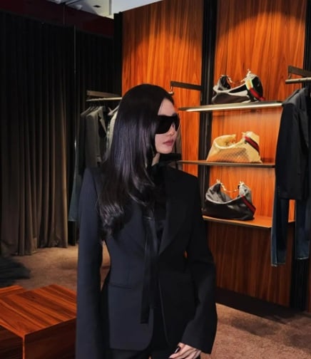 Áo blazer ôm dáng, quần tây đồng điệu, cà vạt lụa đen và kính mát bản lớn – tất cả tạo nên hình ảnh một biểu tượng thời trang quyền lực,